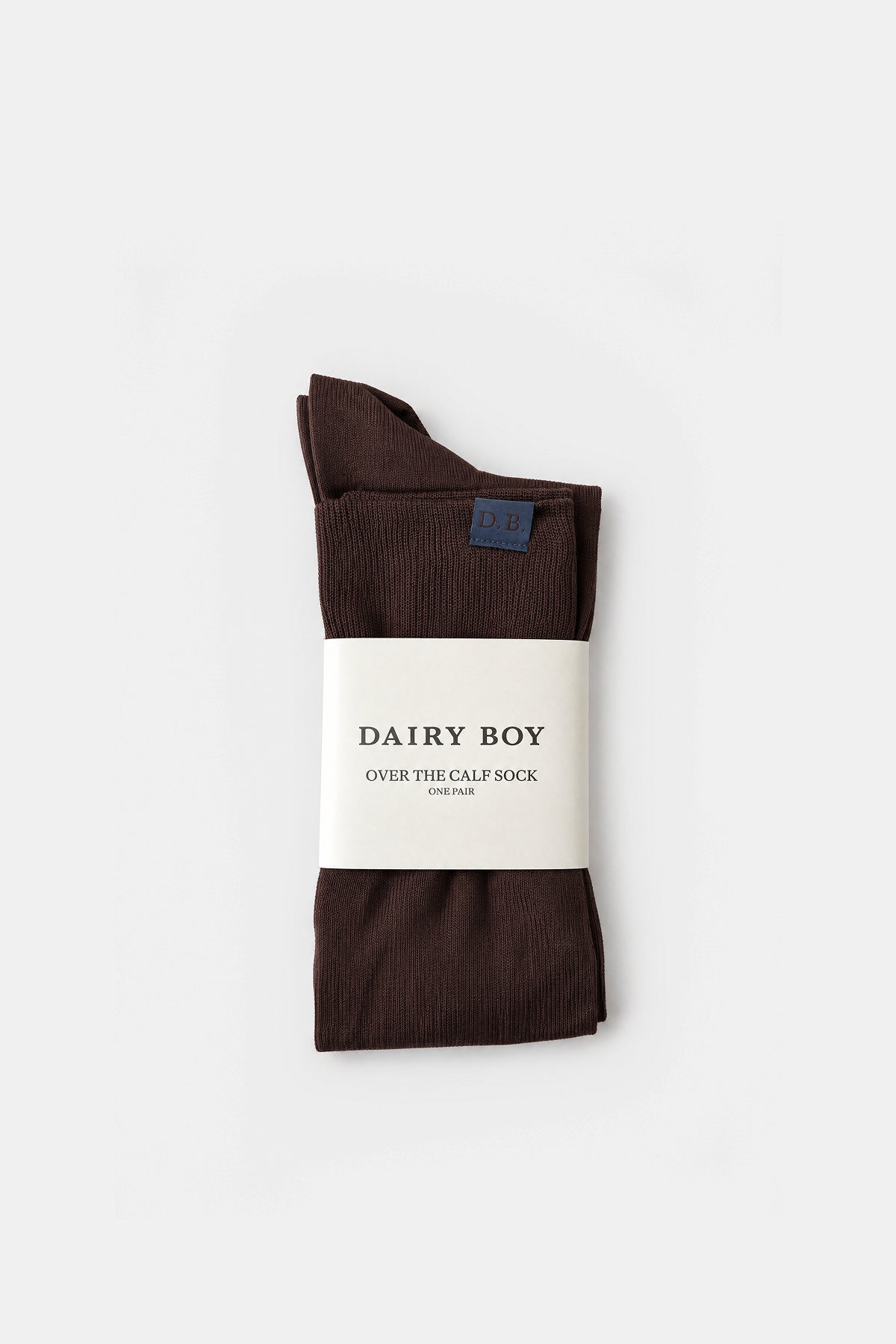 A pair of folded dark brown over-the-calf socks with a white paper label reading 'DAIRY BOY OVER THE CALF SOCK', photographed on a clean white background.