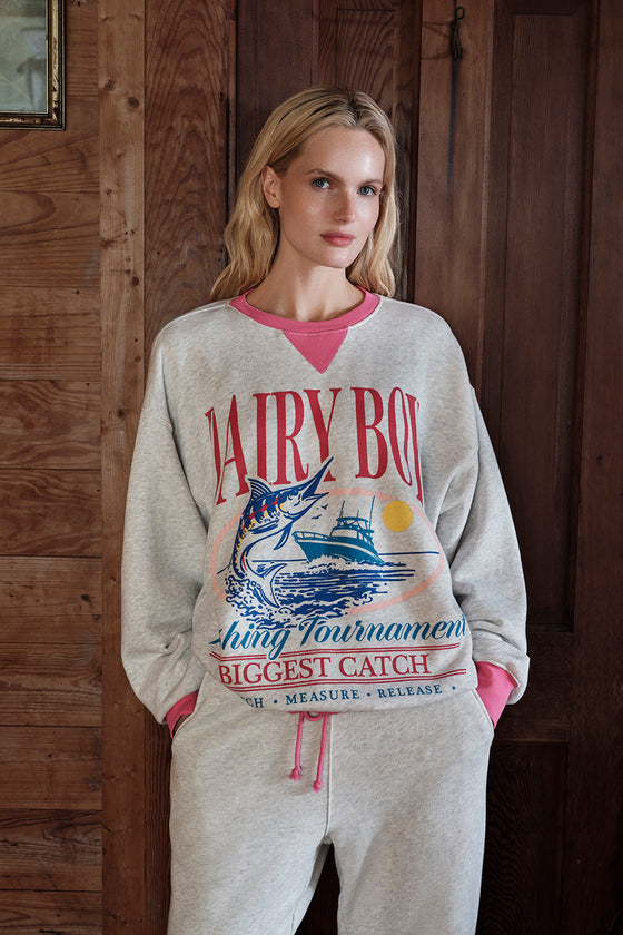 Woman wearing a 'Dairy Boy' sweatshirt with a fish graphic in a rustic setting
|M1