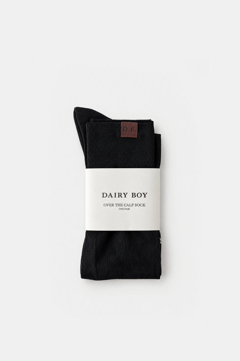 A pair of black over-the-golf socks folded and wrapped in a white paper band labeled 'DAIRY BOY', photographed on a clean light gray background.