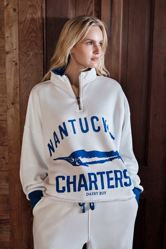 Woman wearing a white tracksuit with 'Nantucket Charters' text and logo against a wooden background |M1