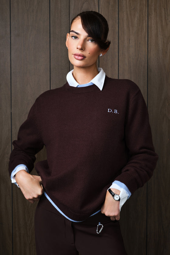A woman models a dark brown knit sweater with a light blue embroidered 'D.B.
|M1