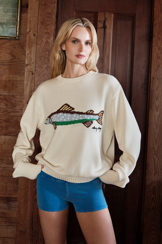 Woman wearing a cream sweater with a fish design in front of a wooden door.
|M1