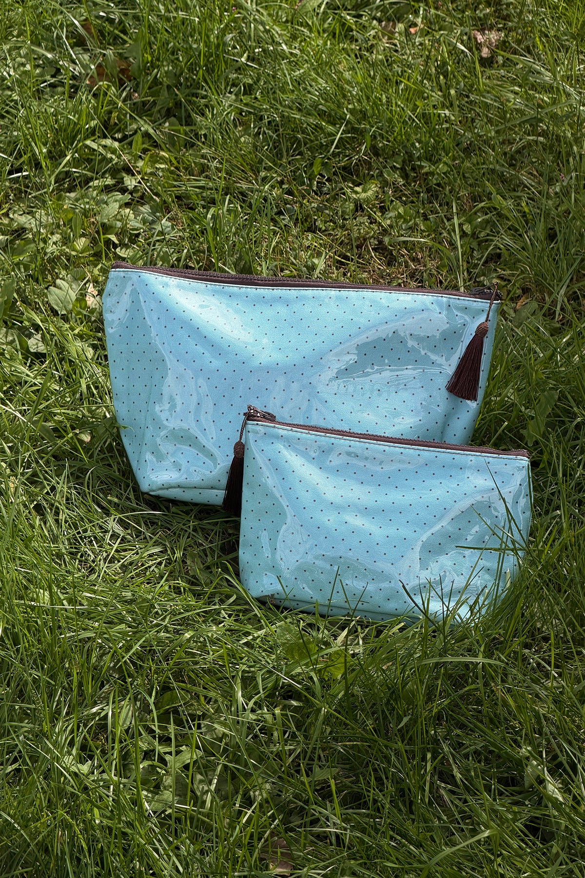 Two glossy light blue makeup bags with small brown polka dots, brown trim and brown tassel zip pulls, in two sizes, front view.
