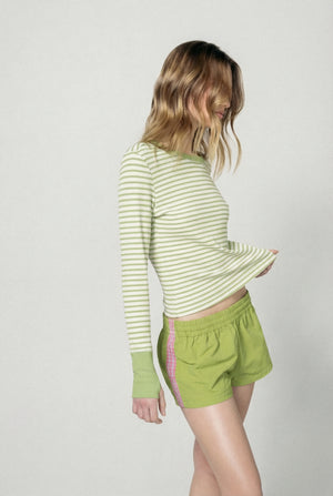 Woman wearing a striped long-sleeve top and green shorts on a plain background |m1
