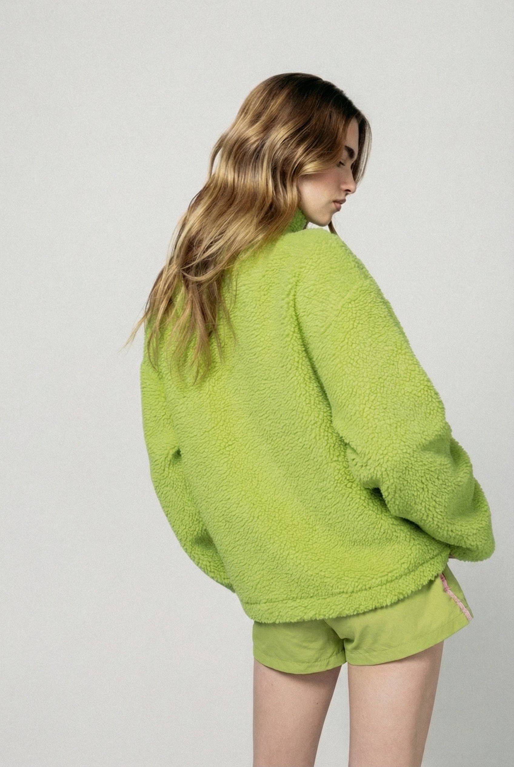 Person wearing a green fleece jacket and shorts on a plain background  |m1