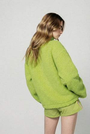 Person wearing a green fleece jacket and shorts on a plain background  |m1