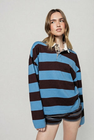 Woman wearing a brown and blue striped rugby shirt with a plain background  |m1