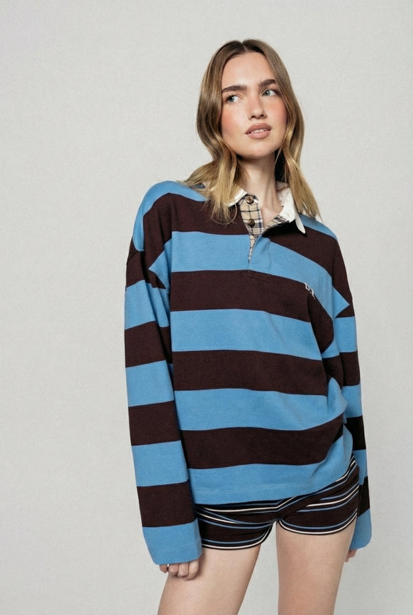 Woman wearing a brown and blue striped rugby shirt with a plain background  |m1