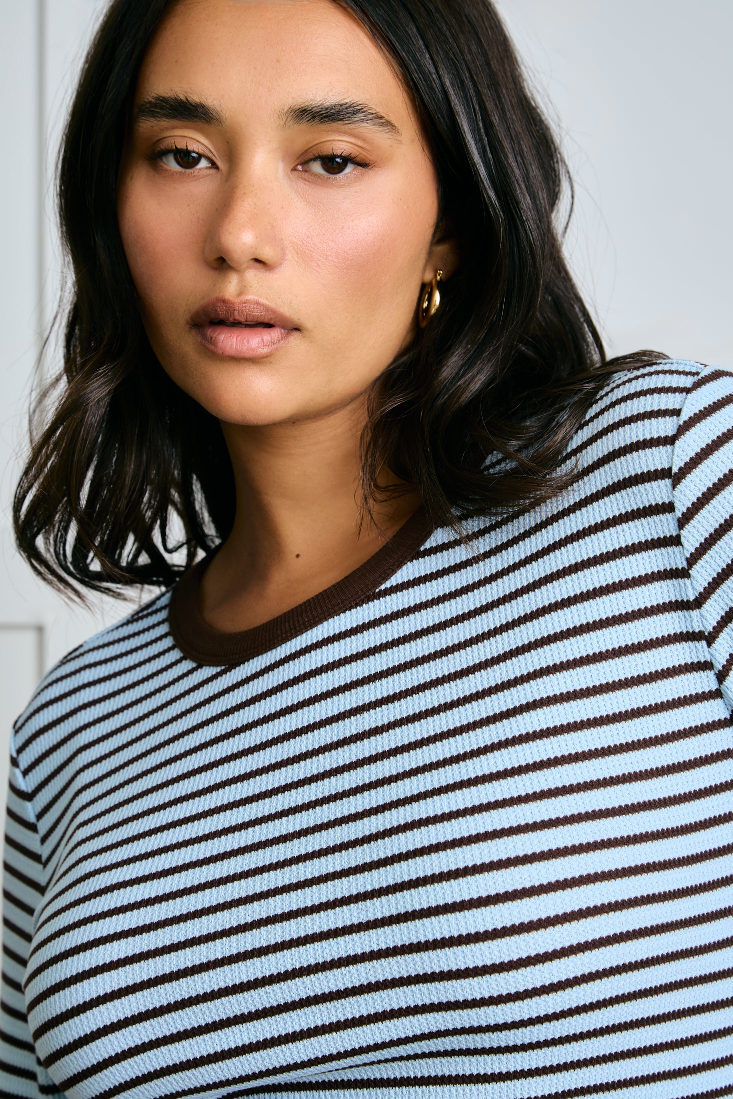 Woman wearing a blue and brown striped long sleeve against a plain background |m1