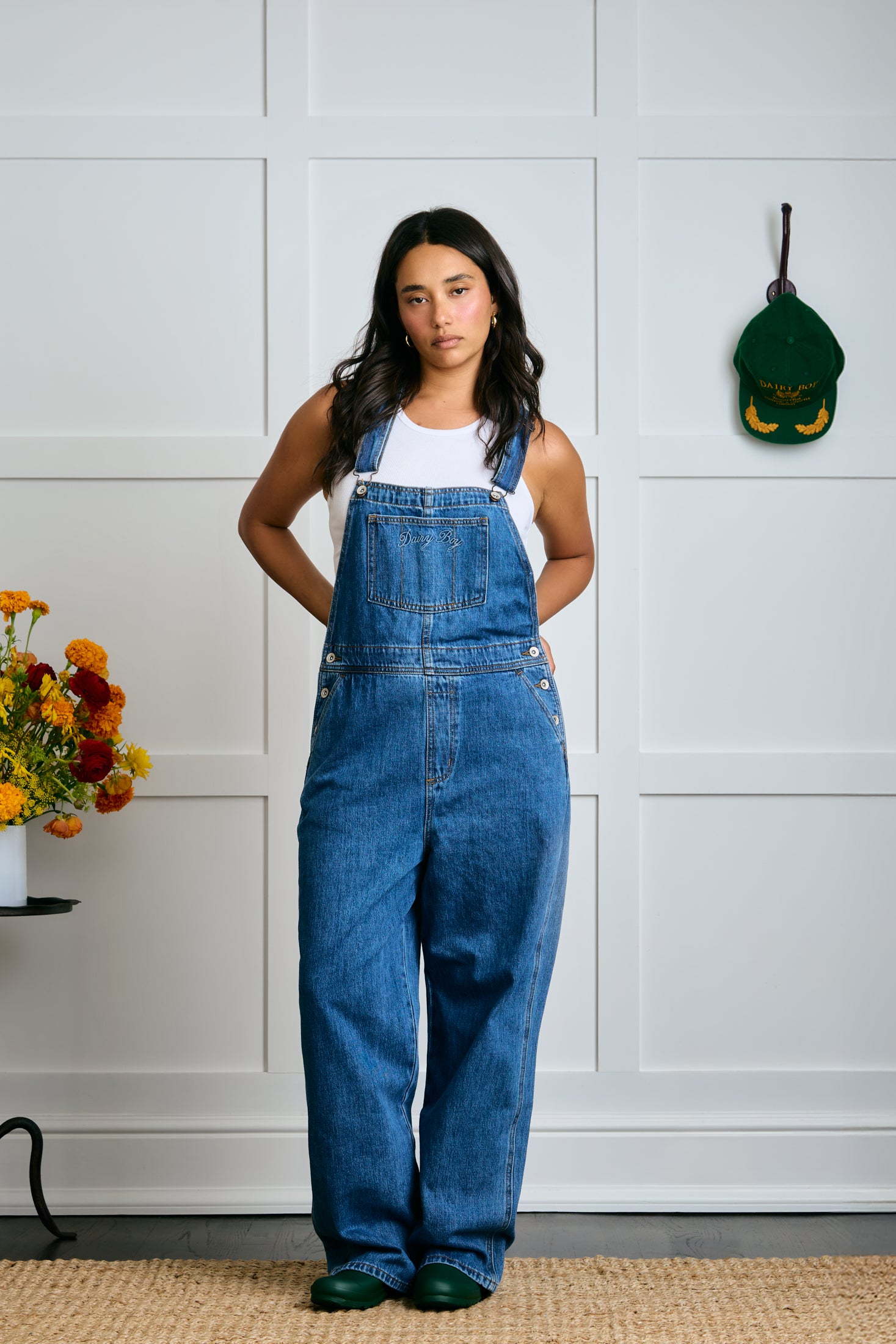 Person wearing blue denim overalls standing in a room with a white paneled wall. |m1