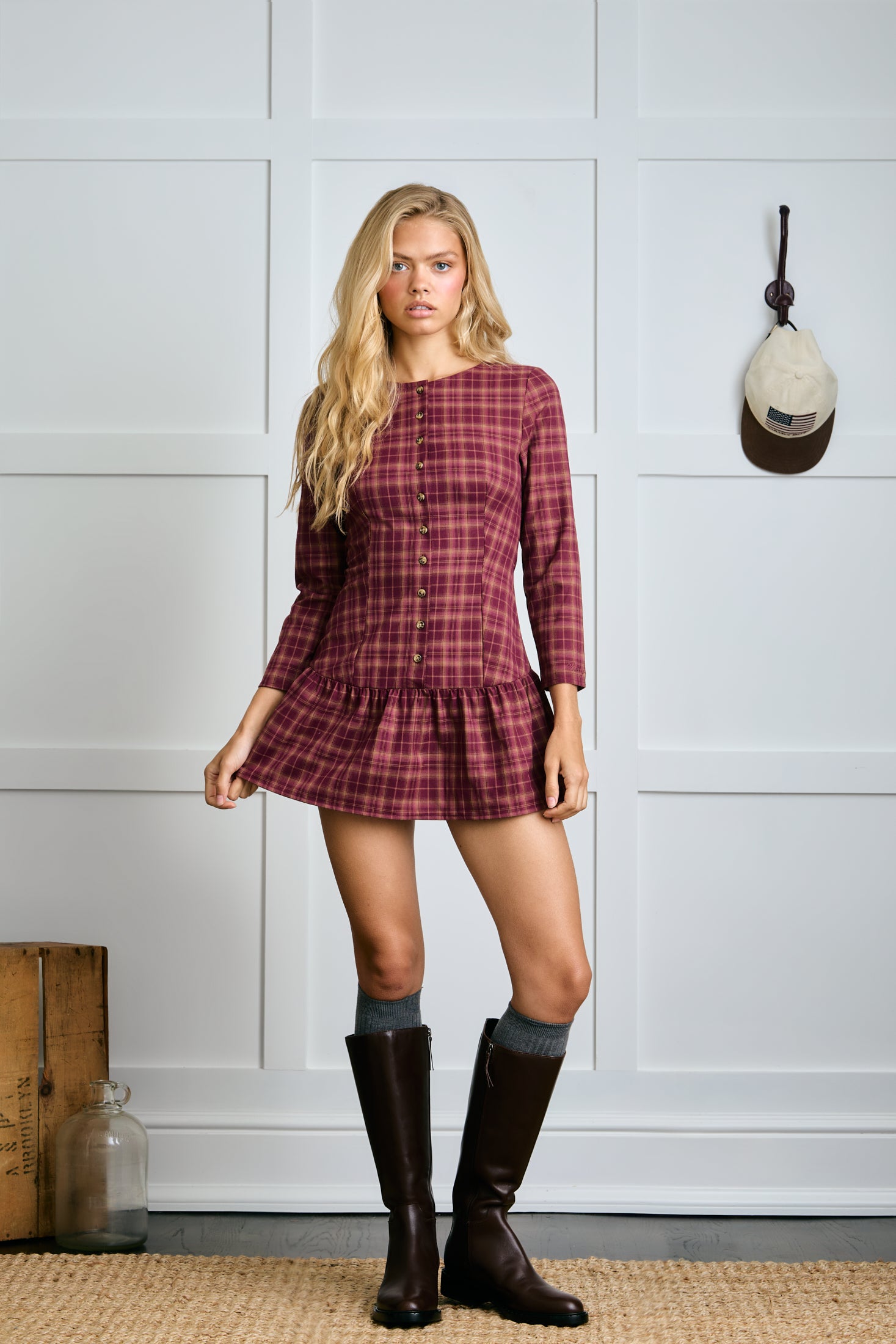 Woman wearing a plaid dress and knee-high boots in a room with a wooden box and decorative item on the wall. |m1