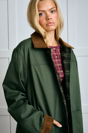 Woman wearing a green jacket with brown collar and cuffs against a white background |m1