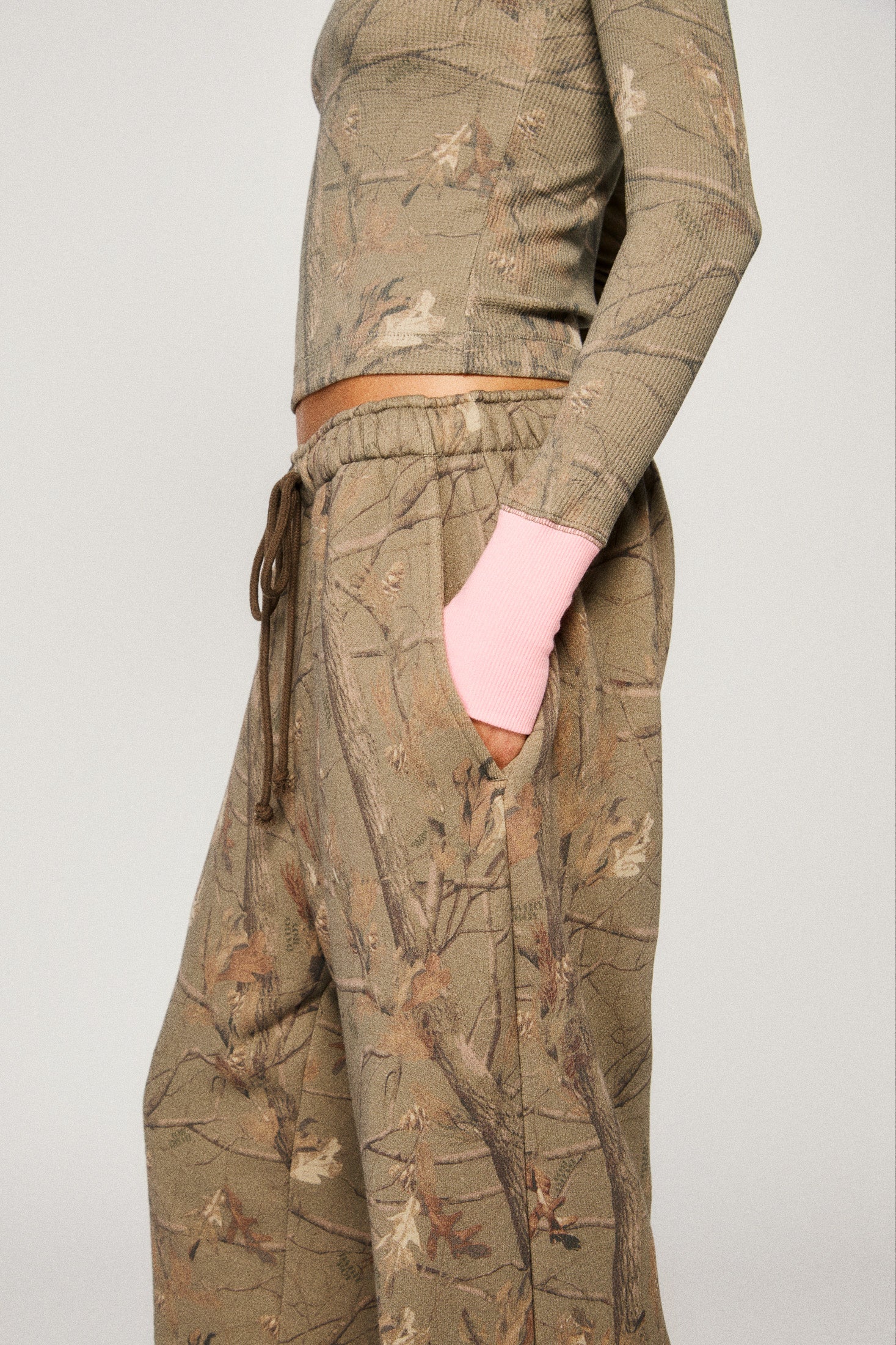 Person wearing a camouflage outfit with a pink sleeve peeking out of a pocket on a plain background |m1