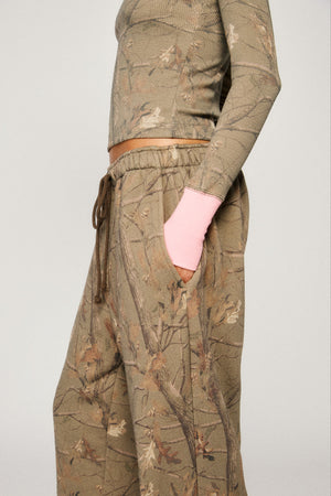 Person wearing a camouflage outfit with a pink sleeve peeking out of a pocket on a plain background |m1