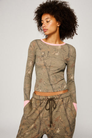 Woman wearing a camouflage long-sleeve top and pants on a plain background |m1