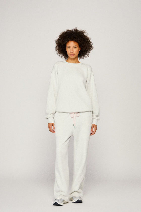 Person wearing a light gray sweater and sweatpants on a plain background |m1