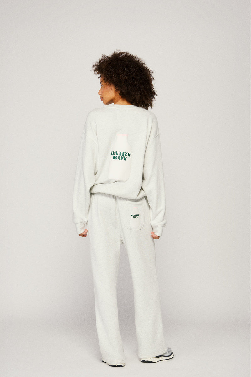 Person wearing a light gray sweatshirt and sweatpants with "Dairy Boy"text on a plain background |m1