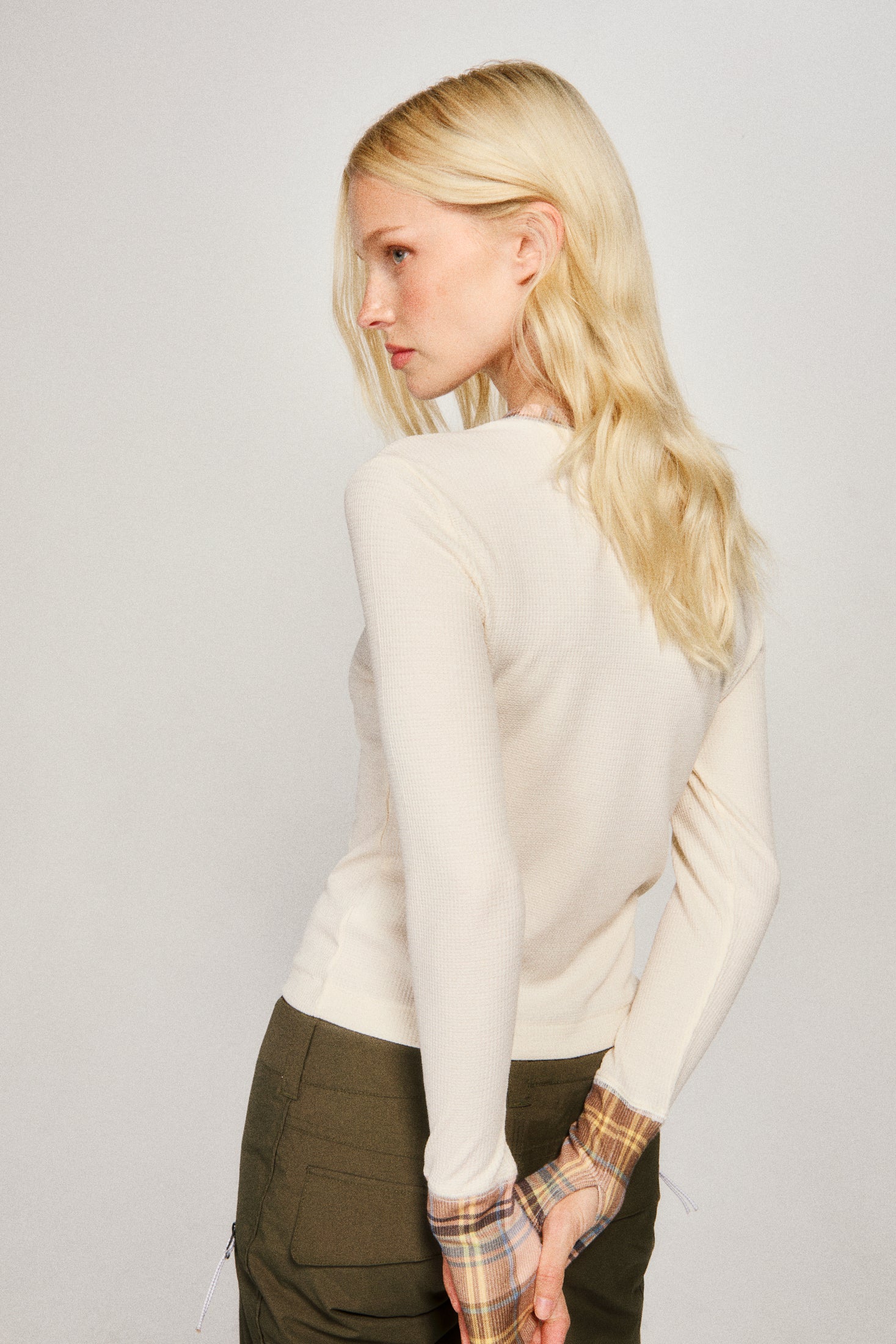 Woman wearing a white sweater and plaid shirt with green pants on a plain background |m2