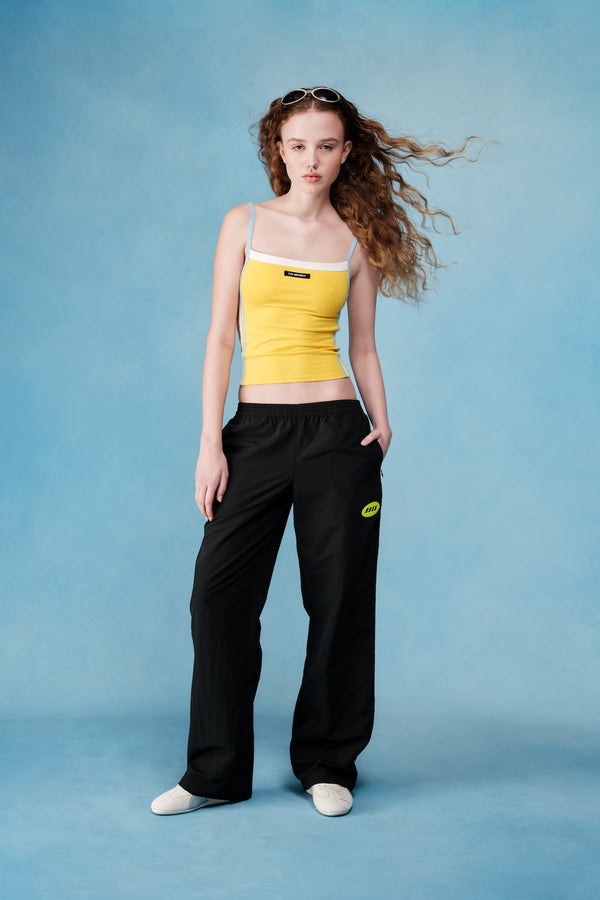 Woman wearing a yellow top and black pants with logos on a blue background  |M1