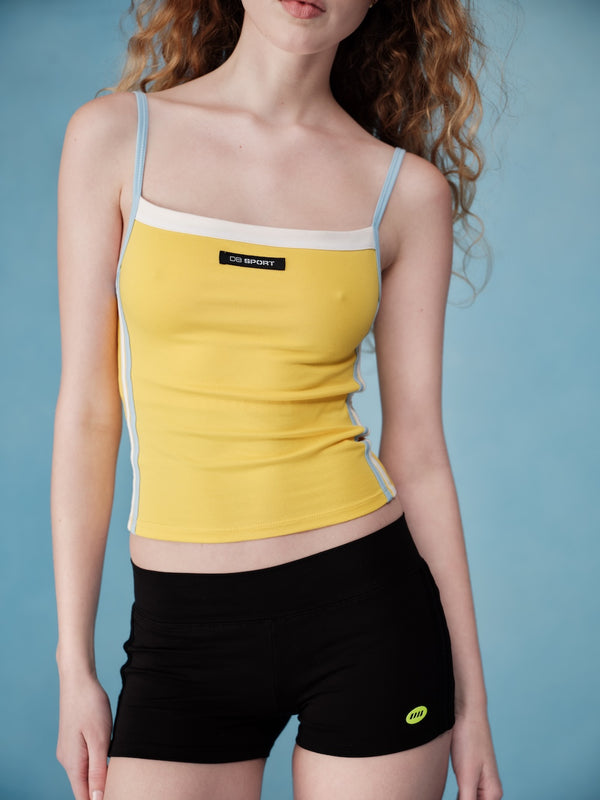 Person wearing a yellow tank top and black shorts against a blue background  |M1