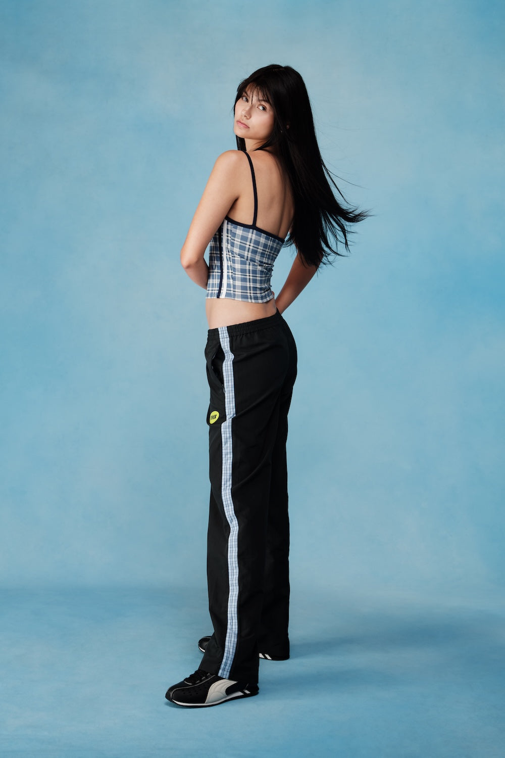 Woman wearing a plaid top and black pants with white stripes against a blue background |M1