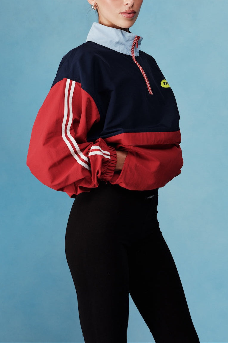 Woman wearing a red and navy tracksuit with a blue background |M1