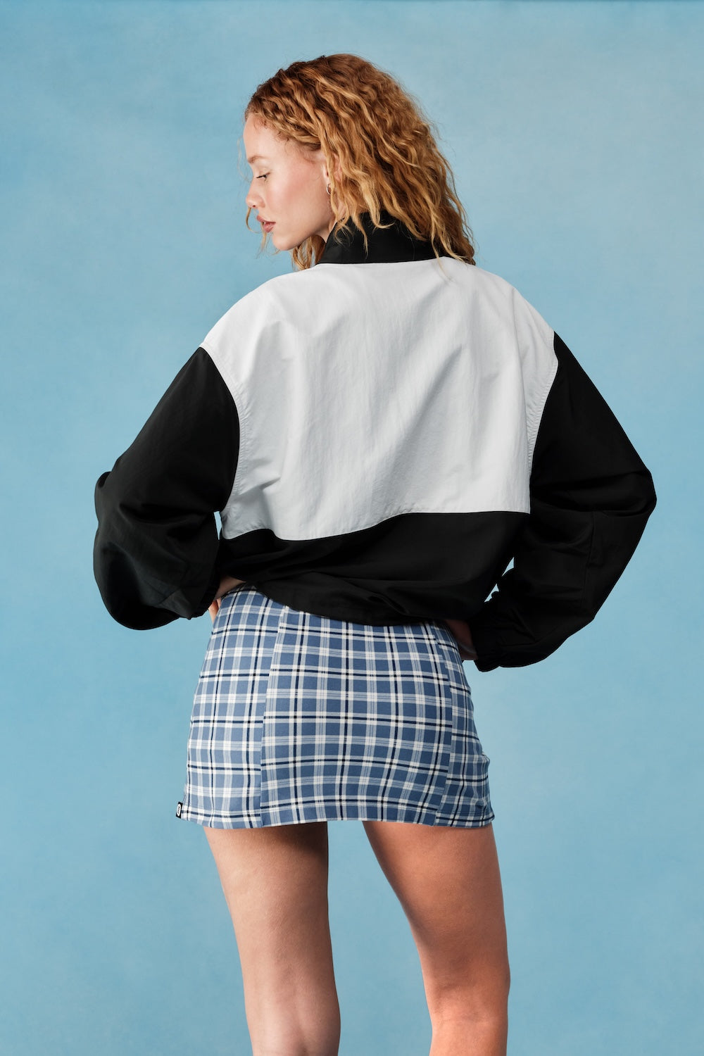 Person wearing a black and white jacket with a blue plaid skirt on a light blue background |M1