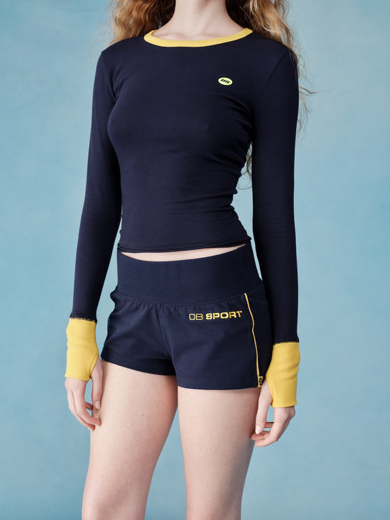 Person wearing a navy long-sleeve top and shorts with yellow accents on a blue background  |M1