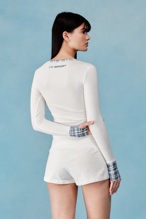 Woman wearing a white long-sleeve top and shorts with plaid cuffs on a light blue background  |M1