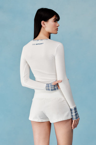 Woman wearing a white long-sleeve top and shorts with plaid cuffs on a light blue background  |M1