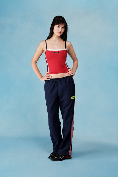 Woman wearing a red tank top and navy pants with red stripes on a blue background |M1