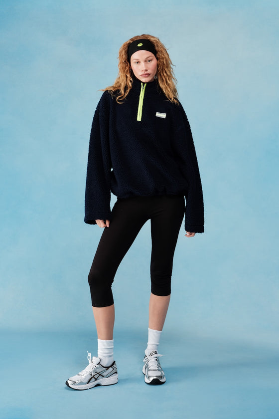 Person wearing a navy fleece with a yellow zipper on a blue background  |M1