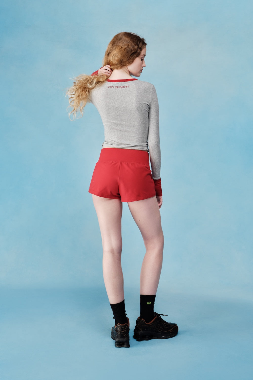 Person wearing a gray long-sleeve shirt and red shorts on a light blue background  |M1