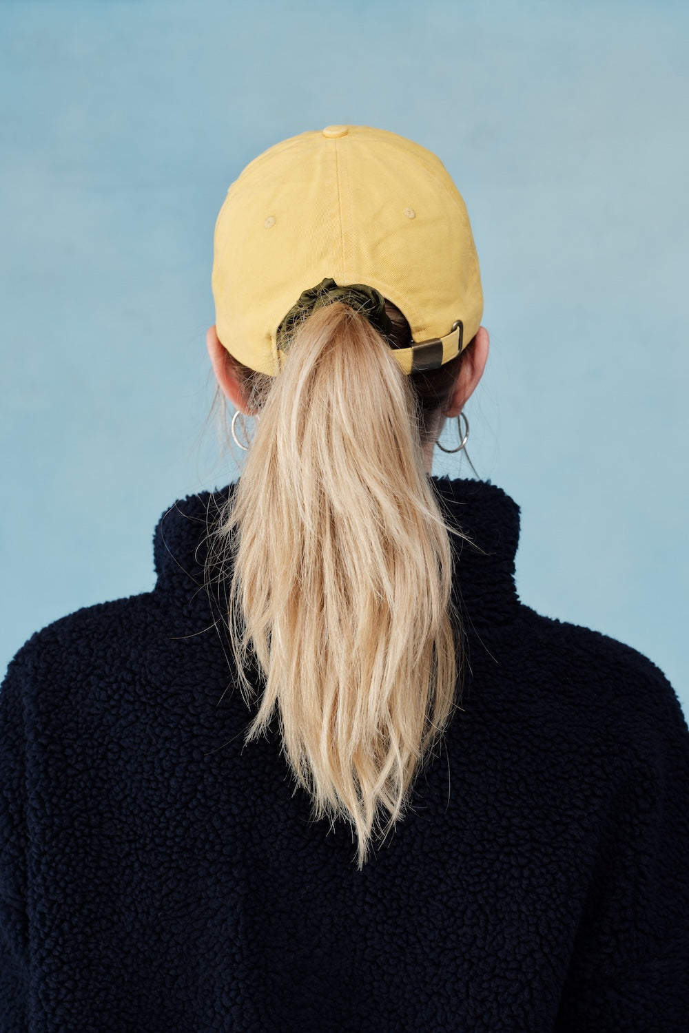 Person wearing a yellow cap and black sweater against a light blue background