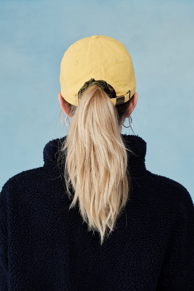 Person wearing a yellow cap and black sweater against a light blue background