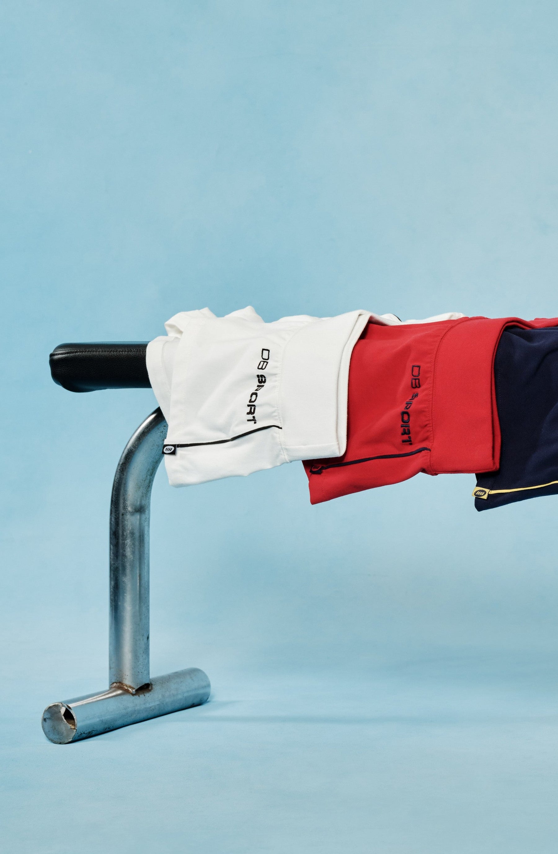 Four pairs of shorts in red, blue, yellow, and white hanging on a metal bar against a light blue background.