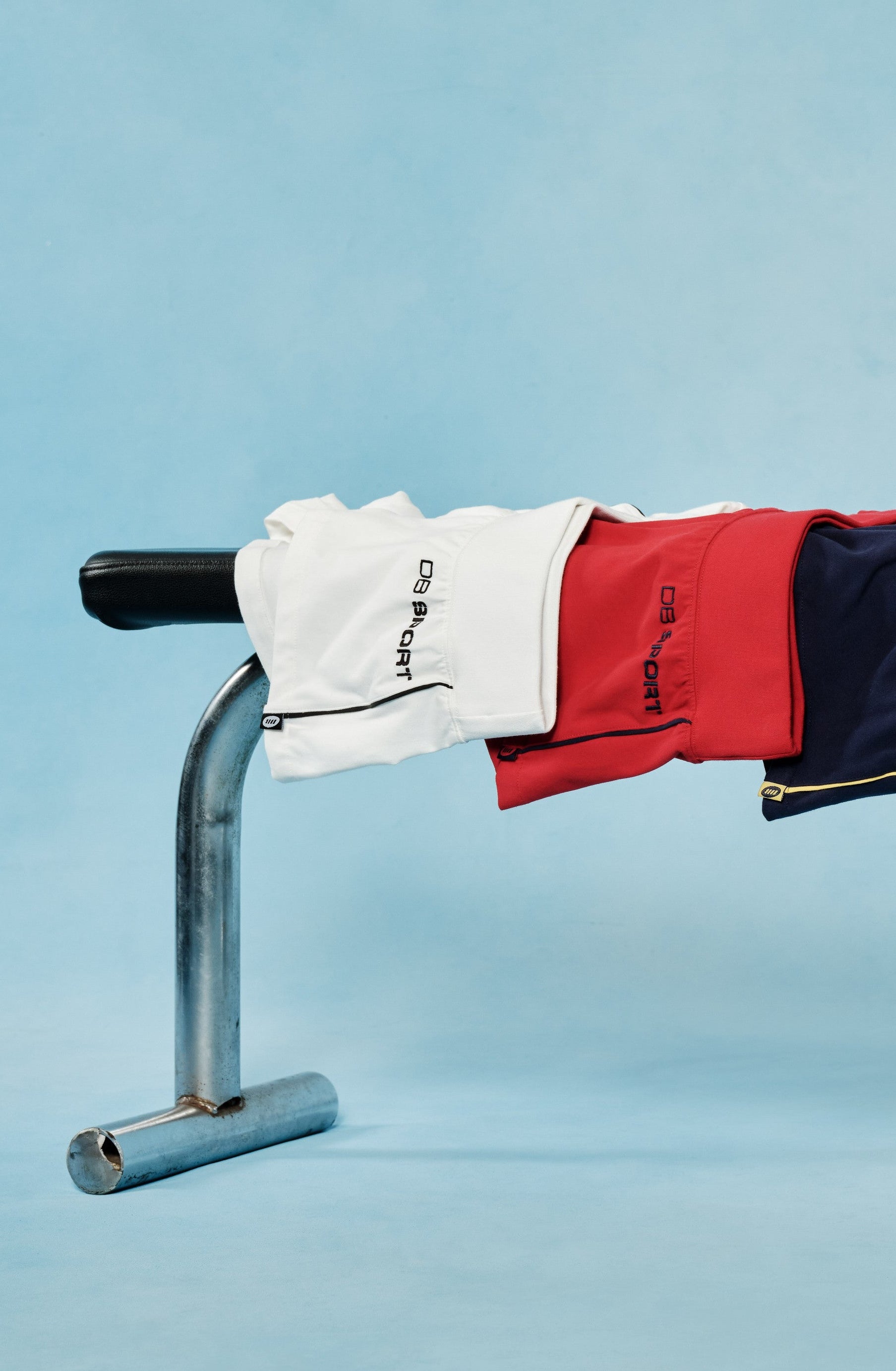 Four pairs of shorts in red, blue, yellow, and white hanging on a metal bar against a light blue background.