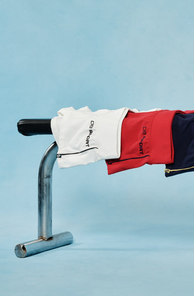 Four pairs of shorts in red, blue, yellow, and white hanging on a metal bar against a light blue background.