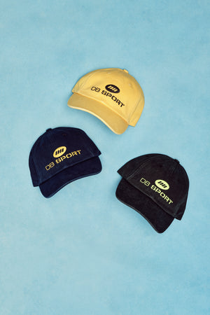 Three caps in yellow, black, and navy on a light blue background with 'DS Sport' branding.