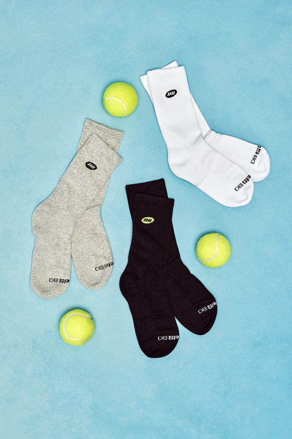 Three pairs of socks in gray, black, and white with tennis balls on a blue background.