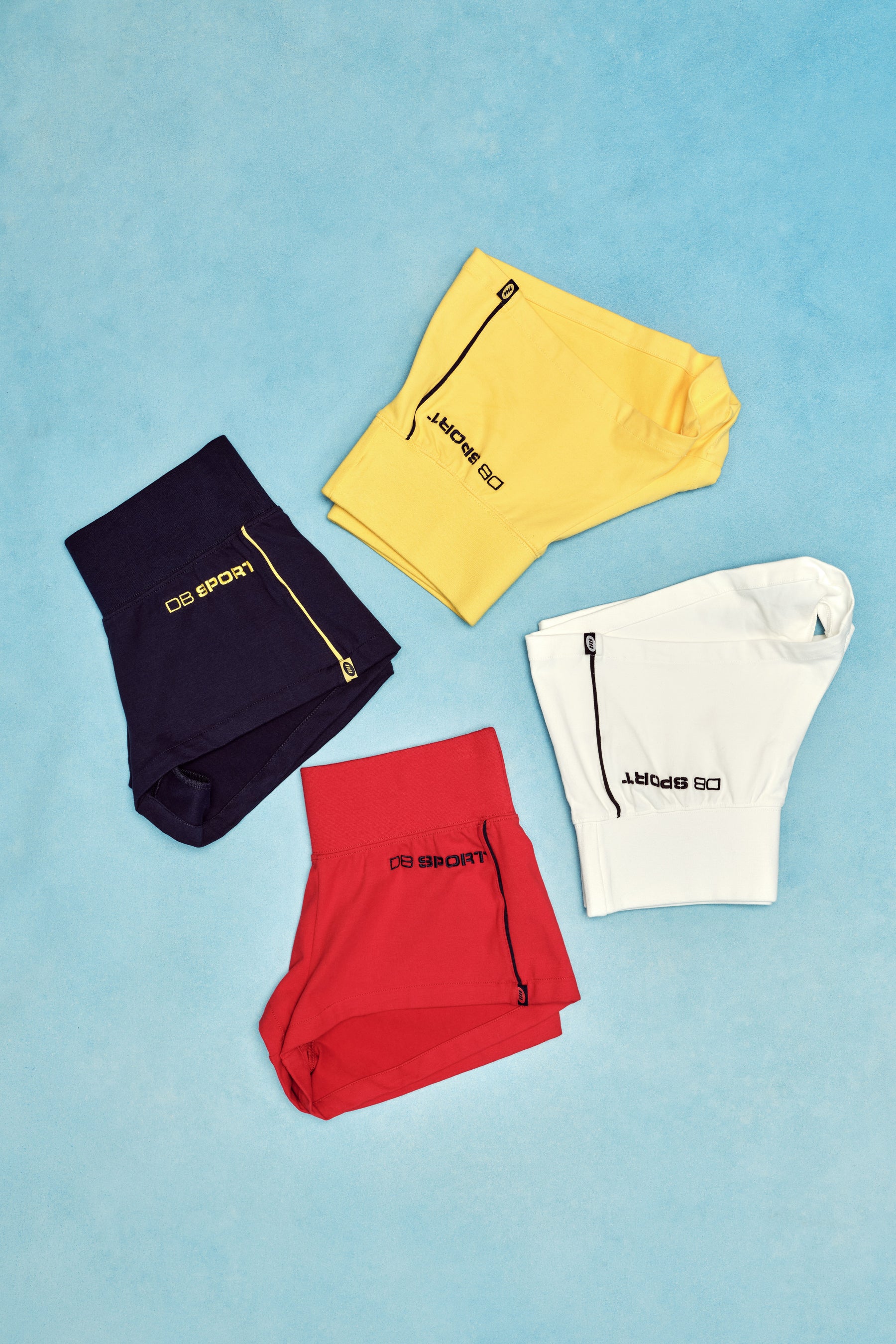 Four pairs of shorts in black, yellow, red, and white on a blue background.