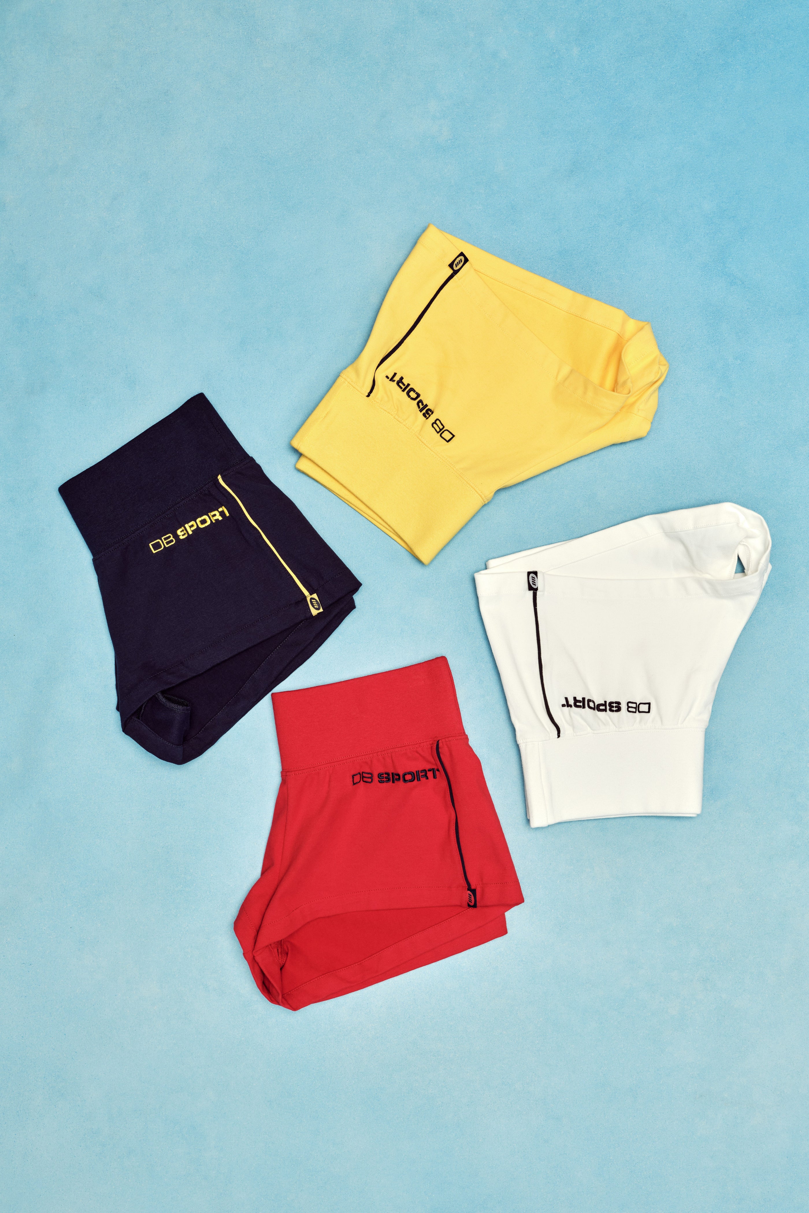 Four pairs of shorts in black, yellow, red, and white on a blue background.