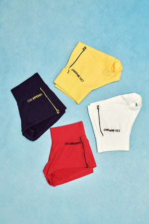 Four pairs of shorts in black, yellow, red, and white on a blue background.
