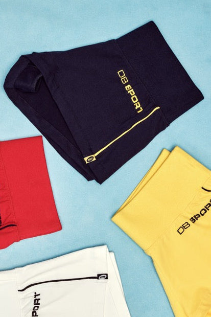 Four pairs of shorts in navy, yellow, red, and white on a blue background.