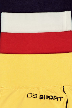 Close-up of a sports outfit with yellow pants, red waistband, and white top, featuring 'DB Sport' branding.