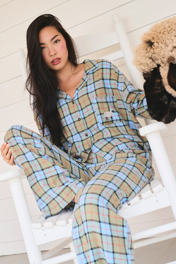 Woman wearing plaid pajamas sitting on a white chair with a white wall. |M1