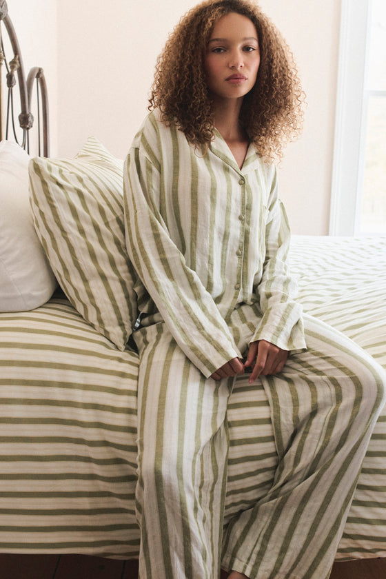 Woman wearing a striped pajama set sitting on a bed. |M1