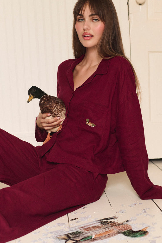 Woman in burgundy pajamas holding a duck on a wooden floor. |M1