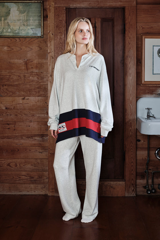 Woman wearing a white tracksuit with red and blue accents in a wooden interior setting.
|M1