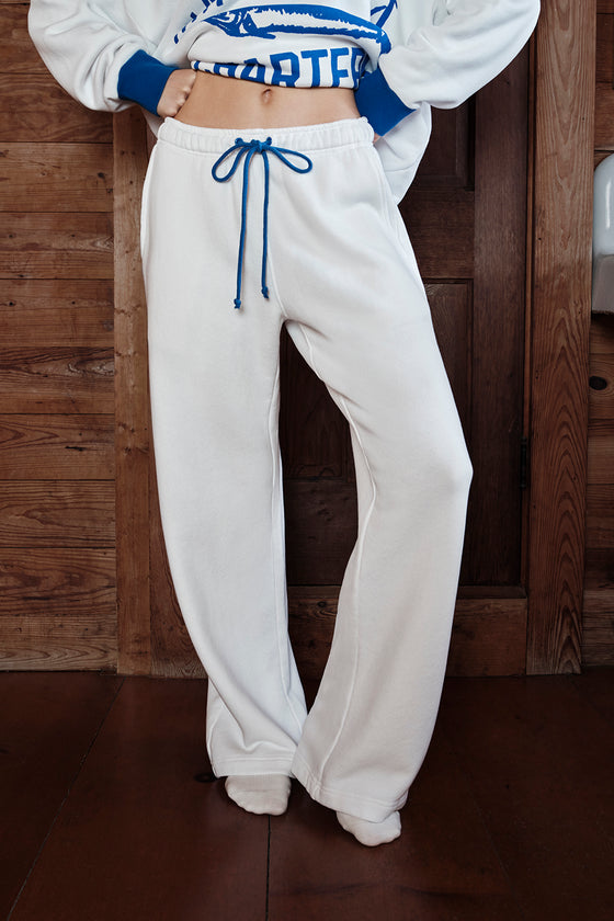 Person wearing a white sweatshirt with blue accents and white sweatpants against a wooden background
|M1